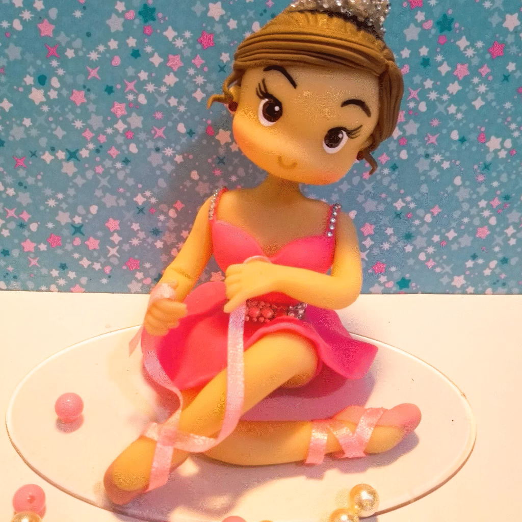 Bailarina em biscuit sentada, de tutu rosa e fita nas sapatilhas, com tiara de strass no cabelo