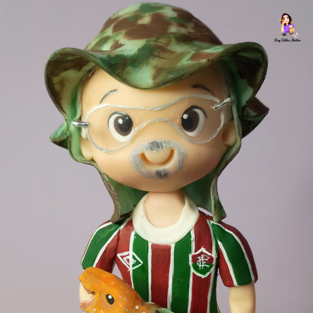 Torcedor do Fluminense de biscuit com chapéu camuflado, óculos e barba grisalha, segurando um peixe