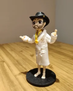 Boneco de biscuit de homem de roupão branco, chapéu preto e fivela dourada, sobre base redonda escura.