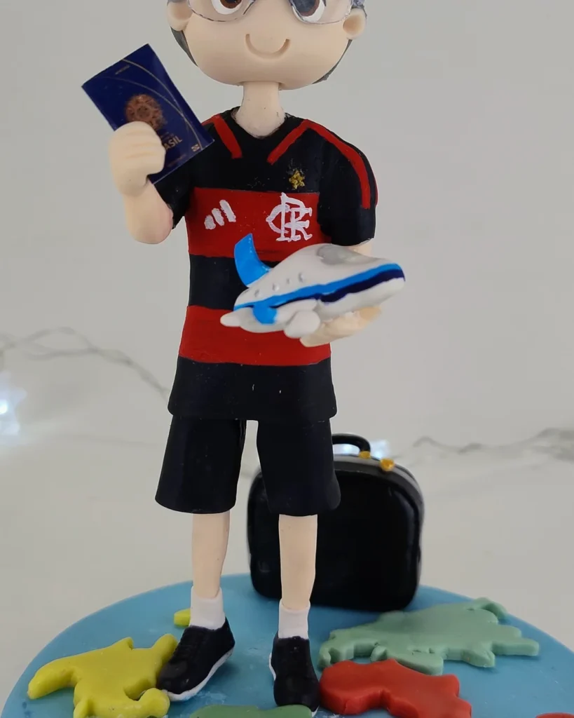 Boneco de biscuit de menino com camisa de time, mala e aviãozinho na mão