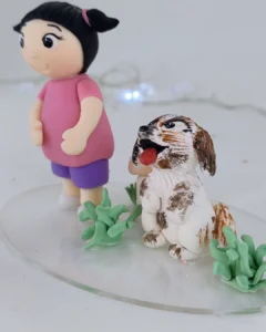 Menina de biscuit de vestido rosa e shorts roxos ao lado de um cachorrinho branco e marrom, entre folhagens verdes.