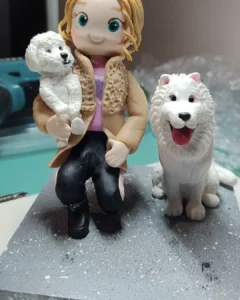 Boneca de biscuit de mulher segurando um cachorro poodle, com outro cachorro branco ao lado