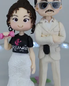 Casal de biscuit: noiva de vestido branco e camiseta preta com halteres, e noivo de terno bege e óculos escuros.
