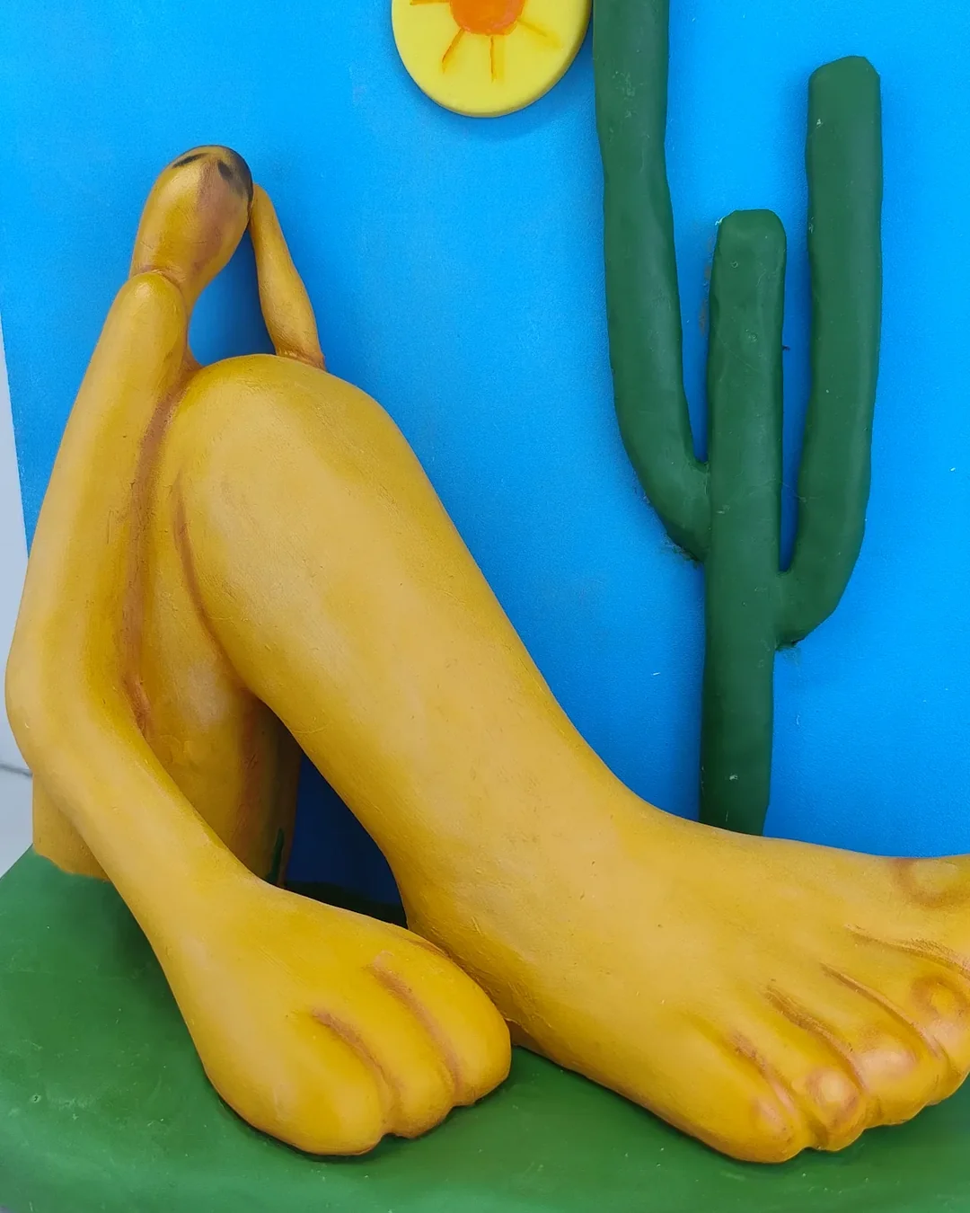 Boneco personalizado de biscuit com a releitura do Abaporu: o pé grande amarelo sobre a base verde, o braço curvado e o cacto