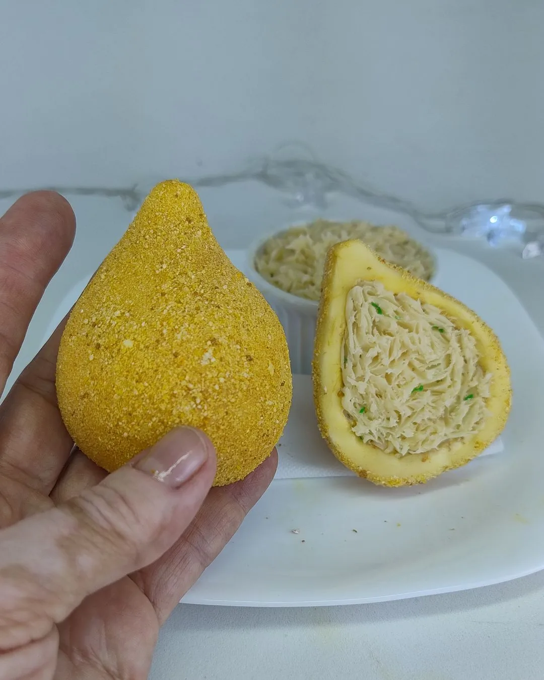 Coxinha de biscuit em formato de gota, com uma metade aberta mostrando o recheio desfiado