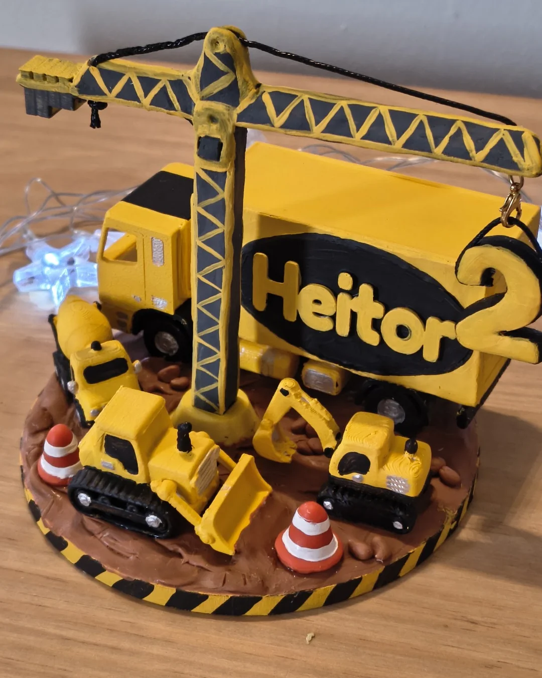 Topo de bolo canteiro de obras em biscuit, com guindaste amarelo erguendo o número 2 ao lado do caminhão do Heitor